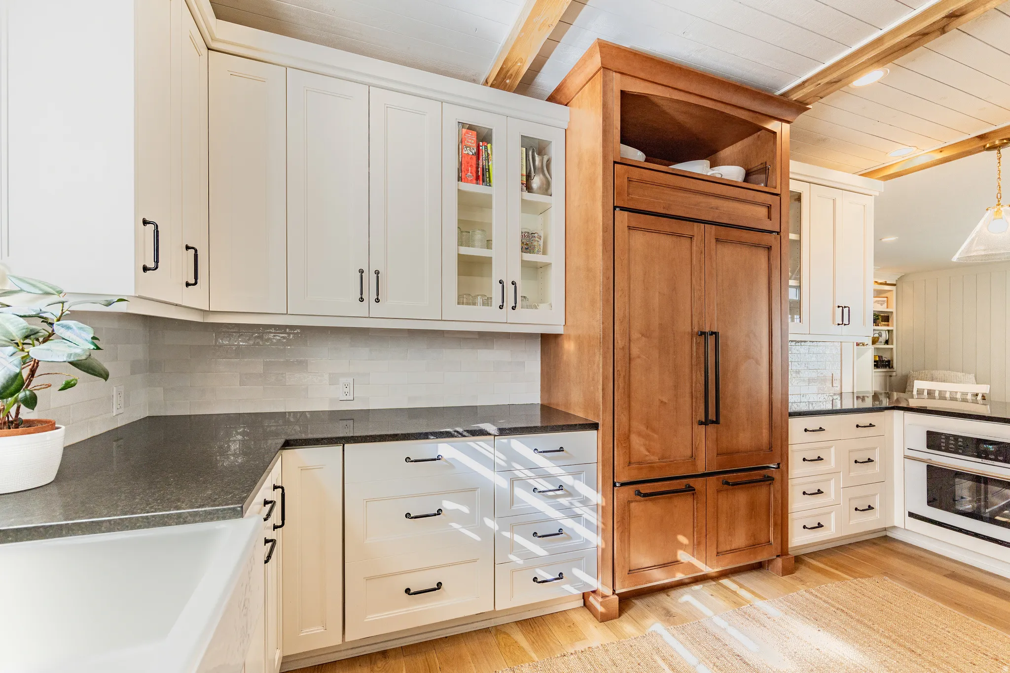 White shaker cabinetry, wood panel refrigerator, dark countertops, tile backsplash, and light wood flooring