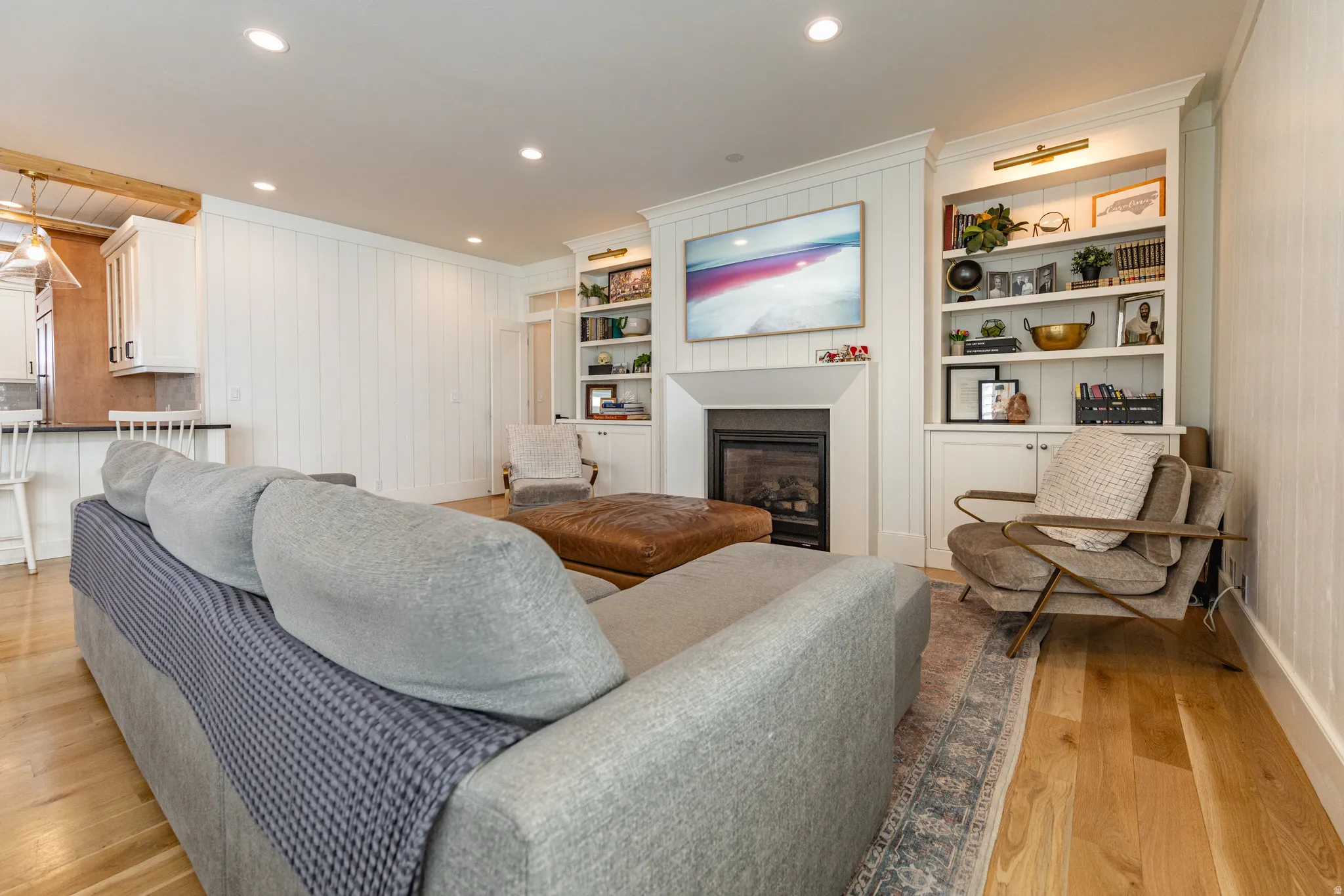 Hardwood flooring, recessed lighting, built-in shelving, white shiplap wall, and a fireplace with a white mantel