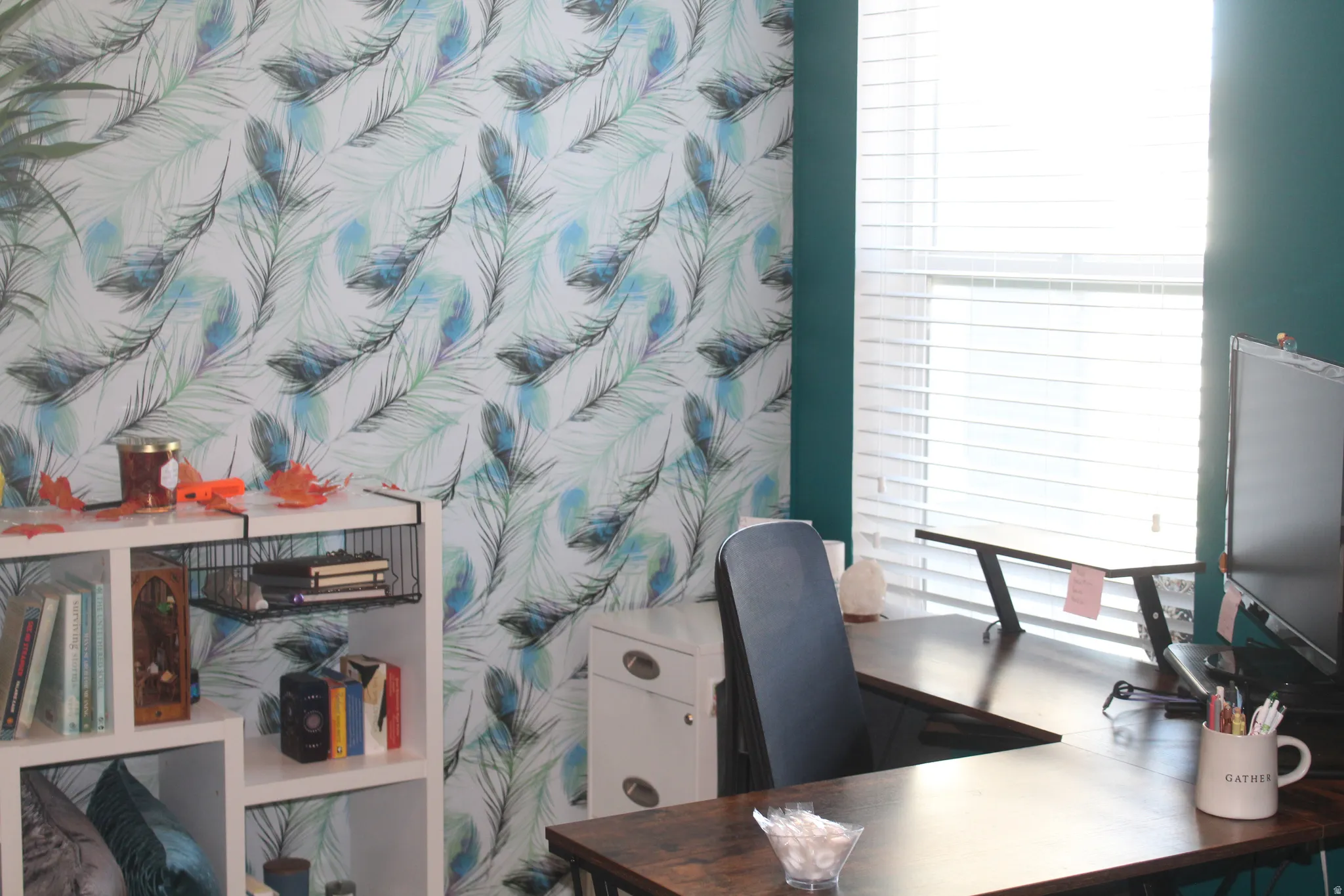 Accent wall with feather pattern wallpaper, white window blinds, and a built-in shelving unit