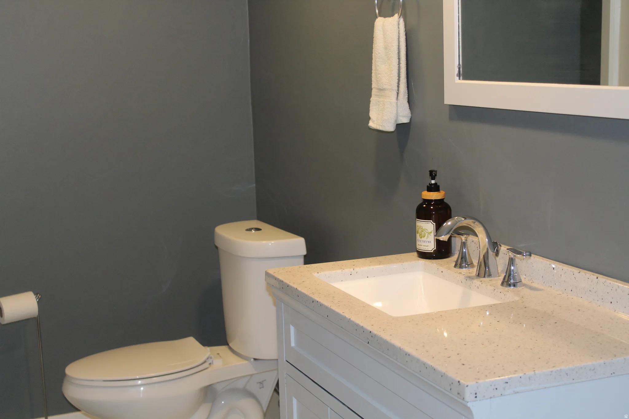 White vanity with a speckled countertop, undermount sink, and chrome-finish faucet