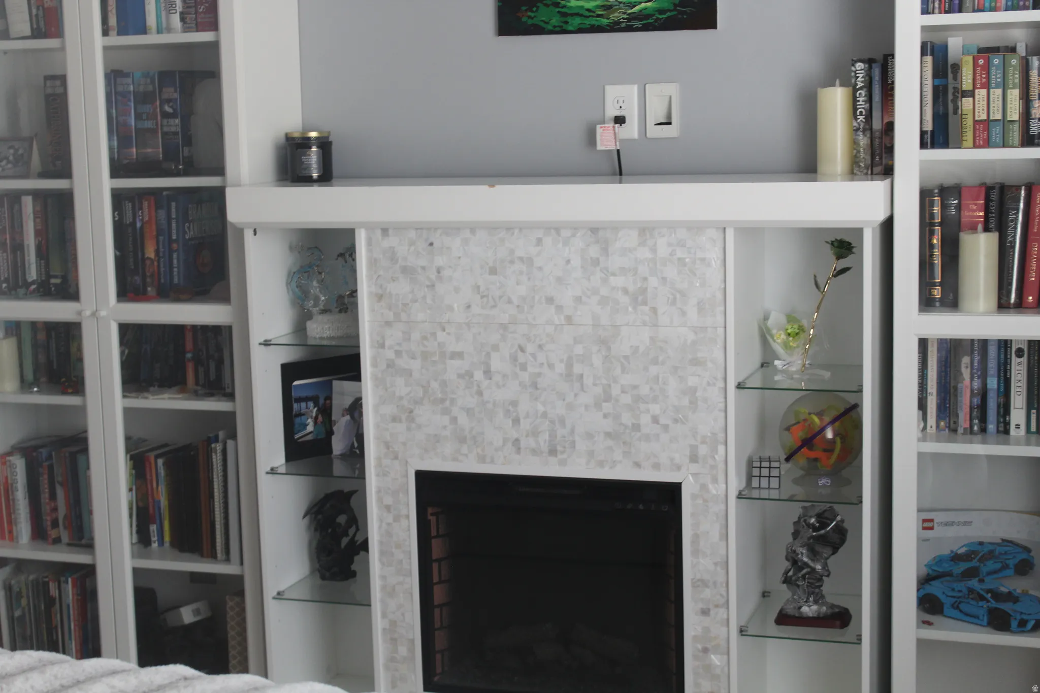 Fireplace with mosaic tile surround, integrated shelving with glass shelves, and built-in white bookcases
