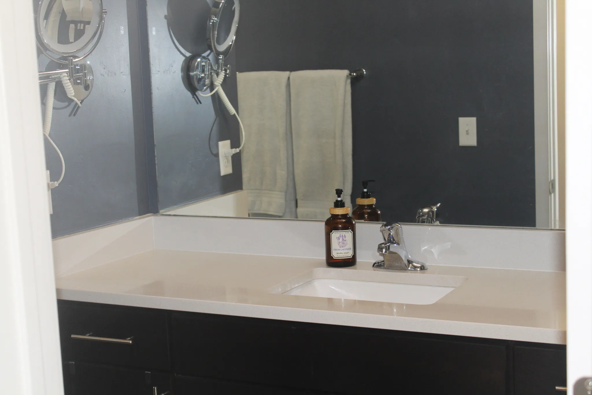 Vanity with an integrated sink, brushed nickel faucet, large mirror, and dark wood-finish cabinetry
