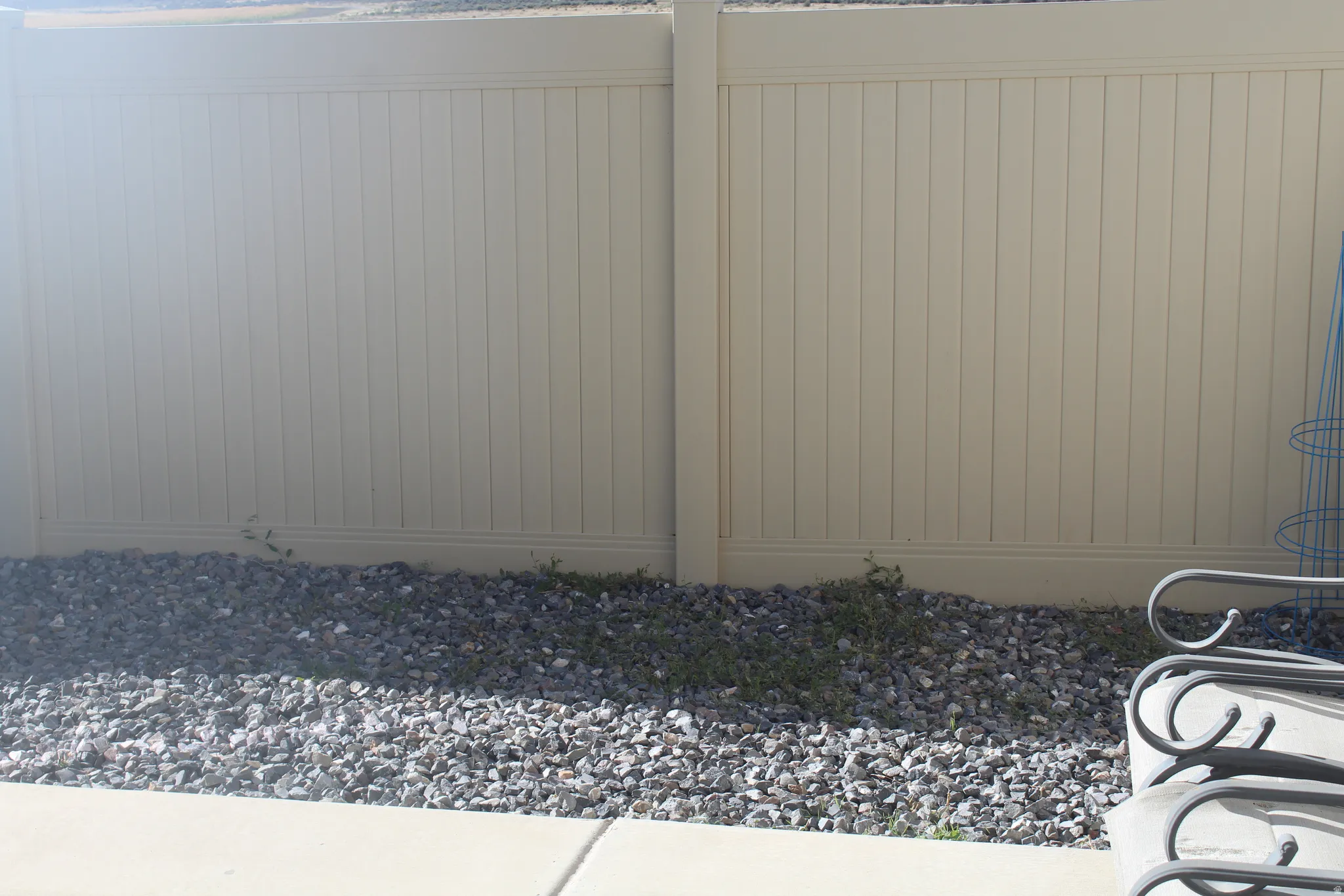 Light-toned privacy fencing with vertical paneling, horizontal top rail, and a decorative base trim, complemented by a gravel ground cover
