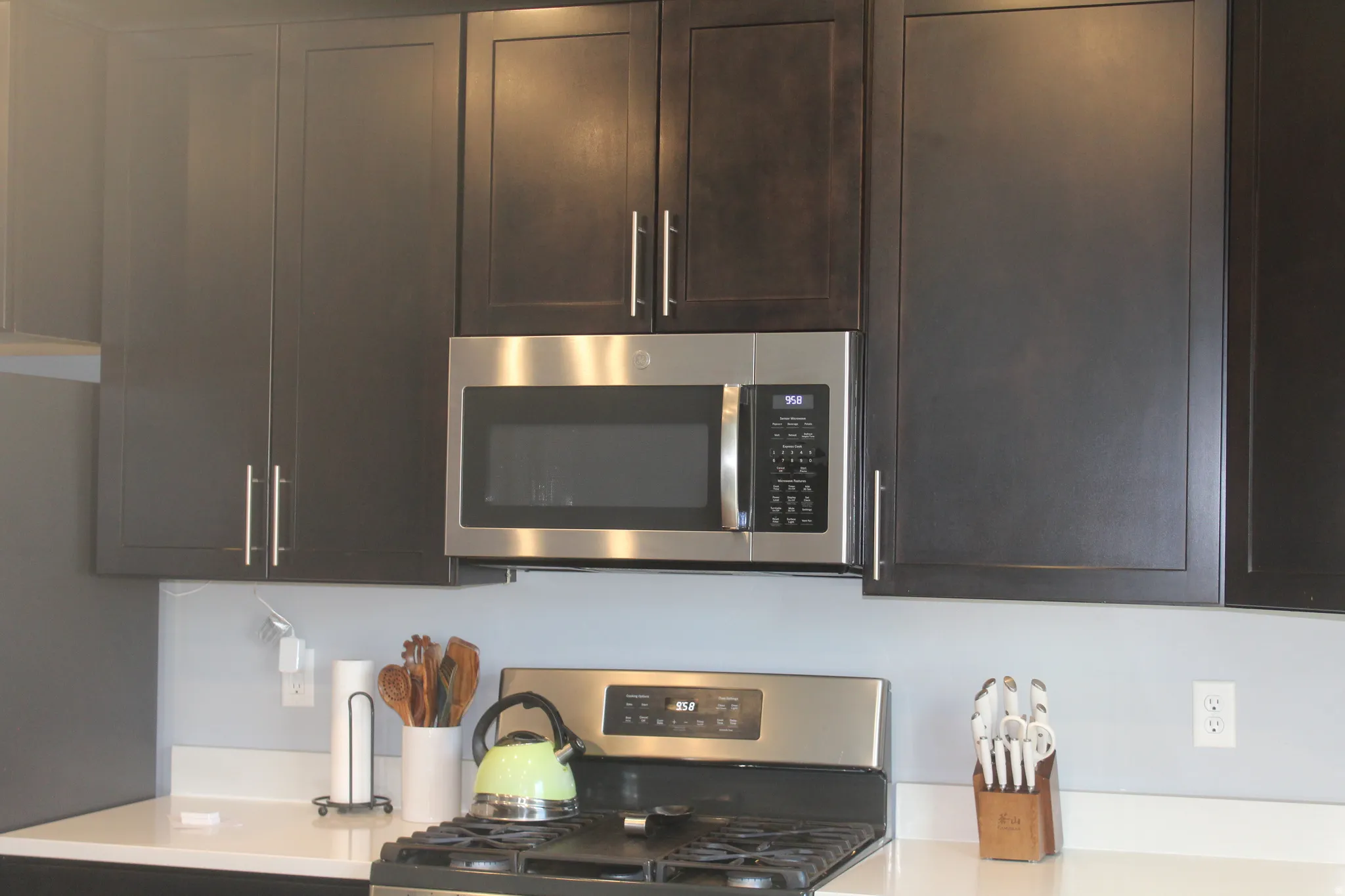 Dark wood-finish cabinetry with brushed nickel hardware, stainless steel microwave, and gas range