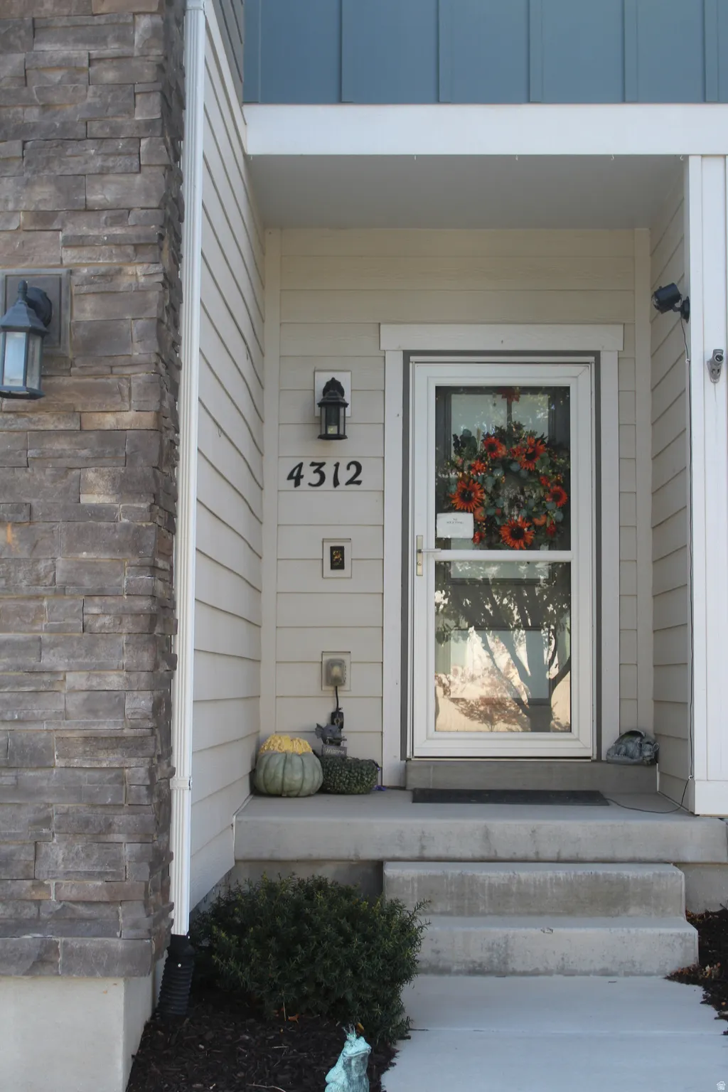 Stone veneer accent column, horizontal siding, covered entry, concrete steps, and a glass-paneled storm door