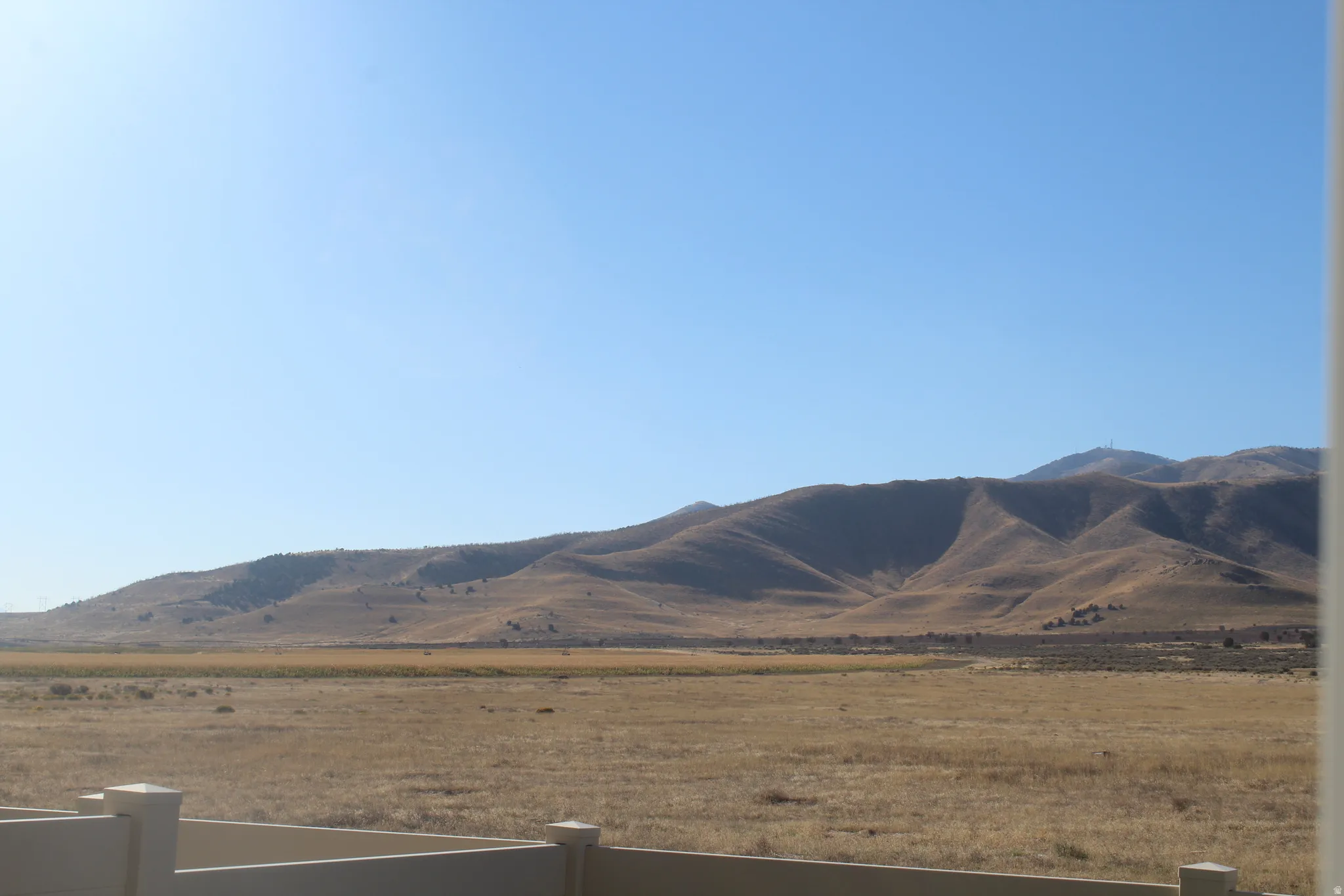 Expansive natural landscape with rolling hills and a clear sky, bordered by a low-profile wall