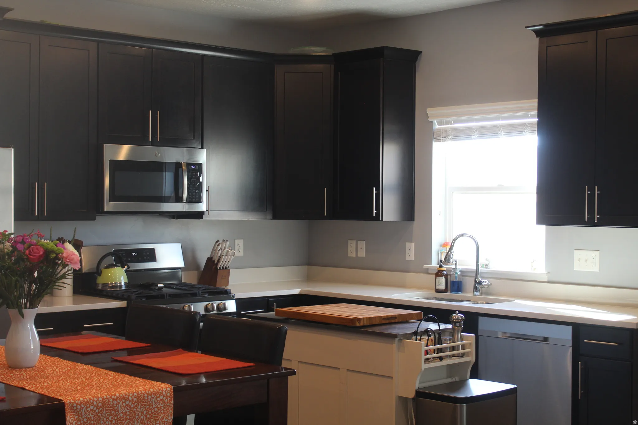 Kitchen featuring dark wood-finish cabinetry, stainless steel appliances, light-toned countertops, and a window above the sink
