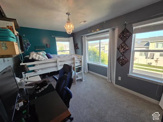 Textured wall paneling, two large windows, an overhead crystal chandelier, and neutral-toned carpeting