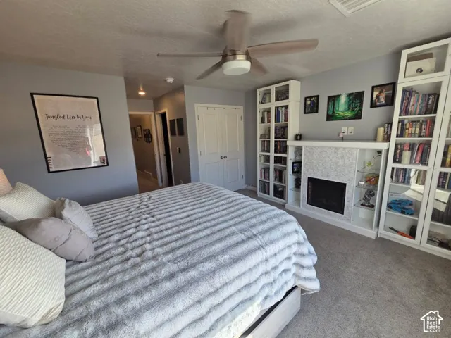 Carpeted bedroom featuring a ceiling fan, built-in fireplace with a tiled surround, and integrated shelving units