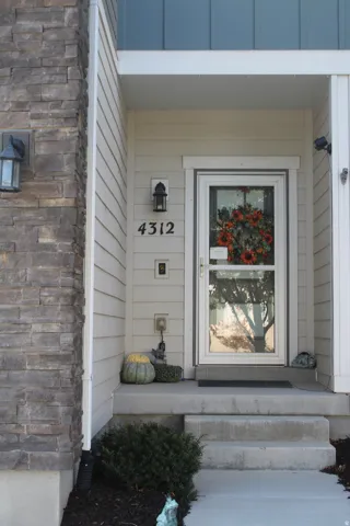 Stone veneer accent column, horizontal siding, covered entry, concrete steps, and a glass-paneled storm door