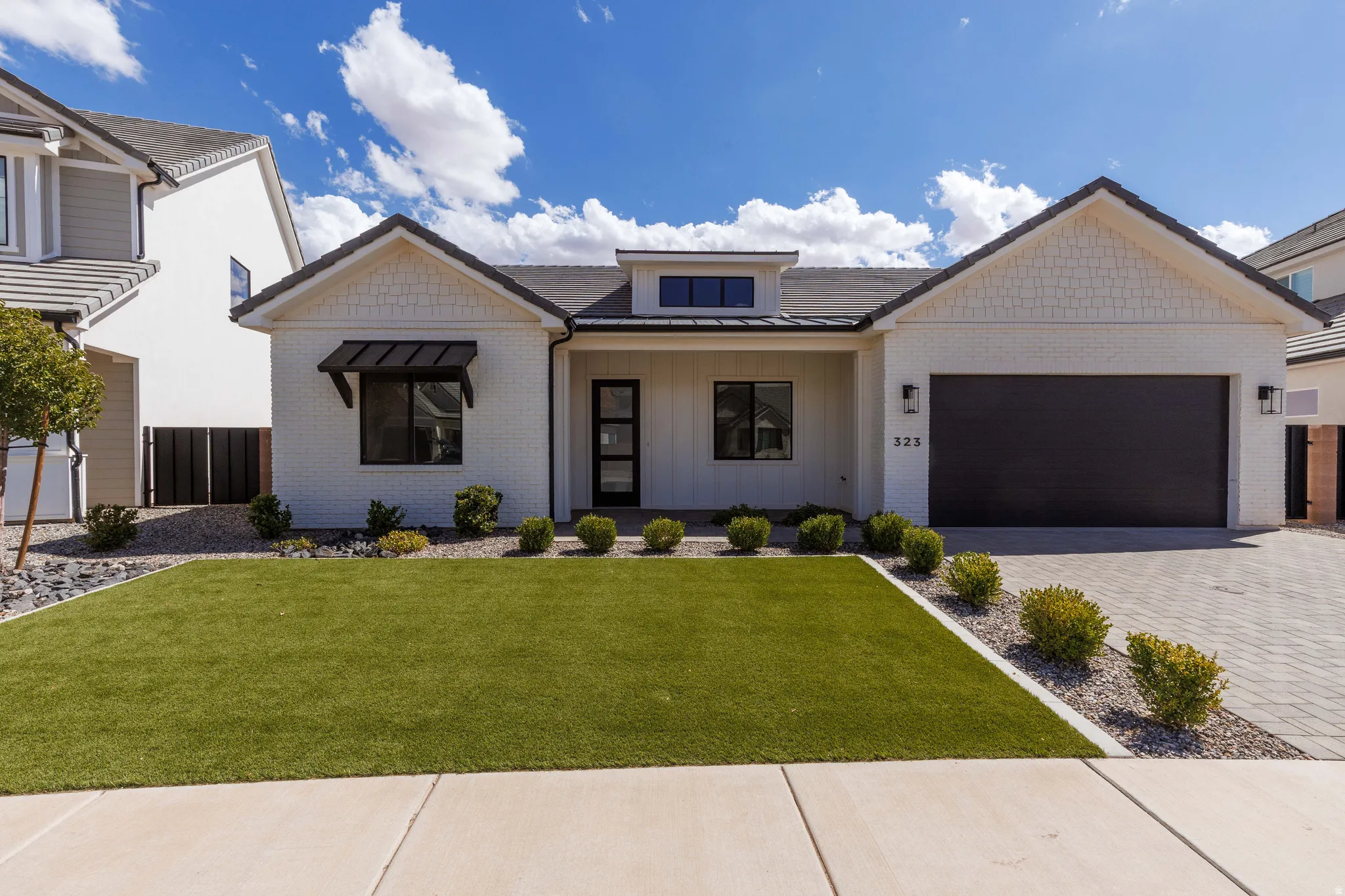 Contemporary exterior with white brick facade, dark-framed windows, a black garage door, paved driveway, and manicured artificial turf