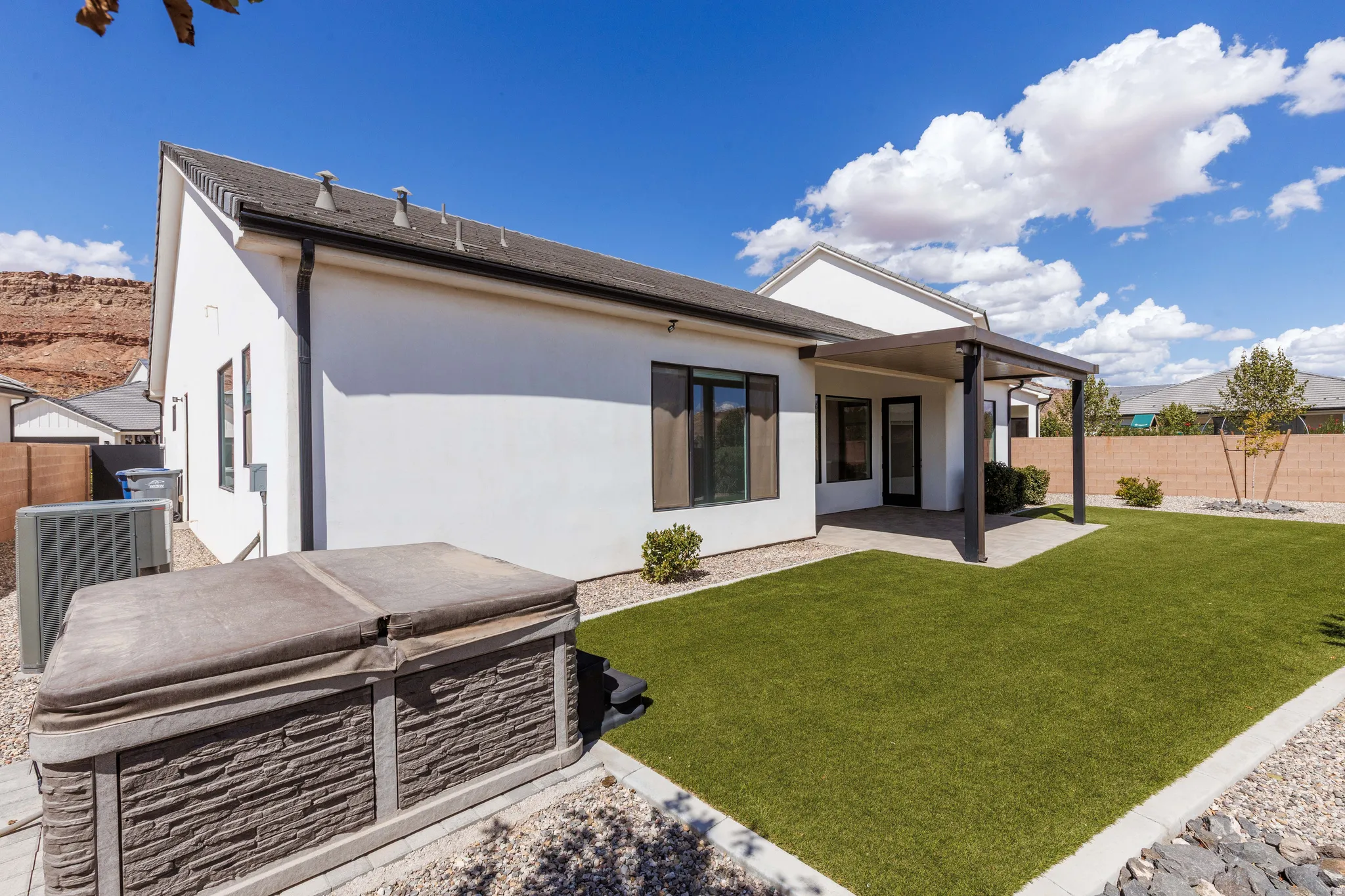 White stucco exterior, covered patio, artificial turf, rock landscaping, and hot tub