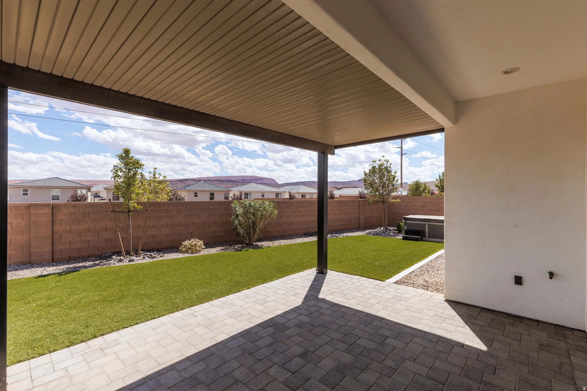 Covered patio with paver flooring, artificial turf, and block wall