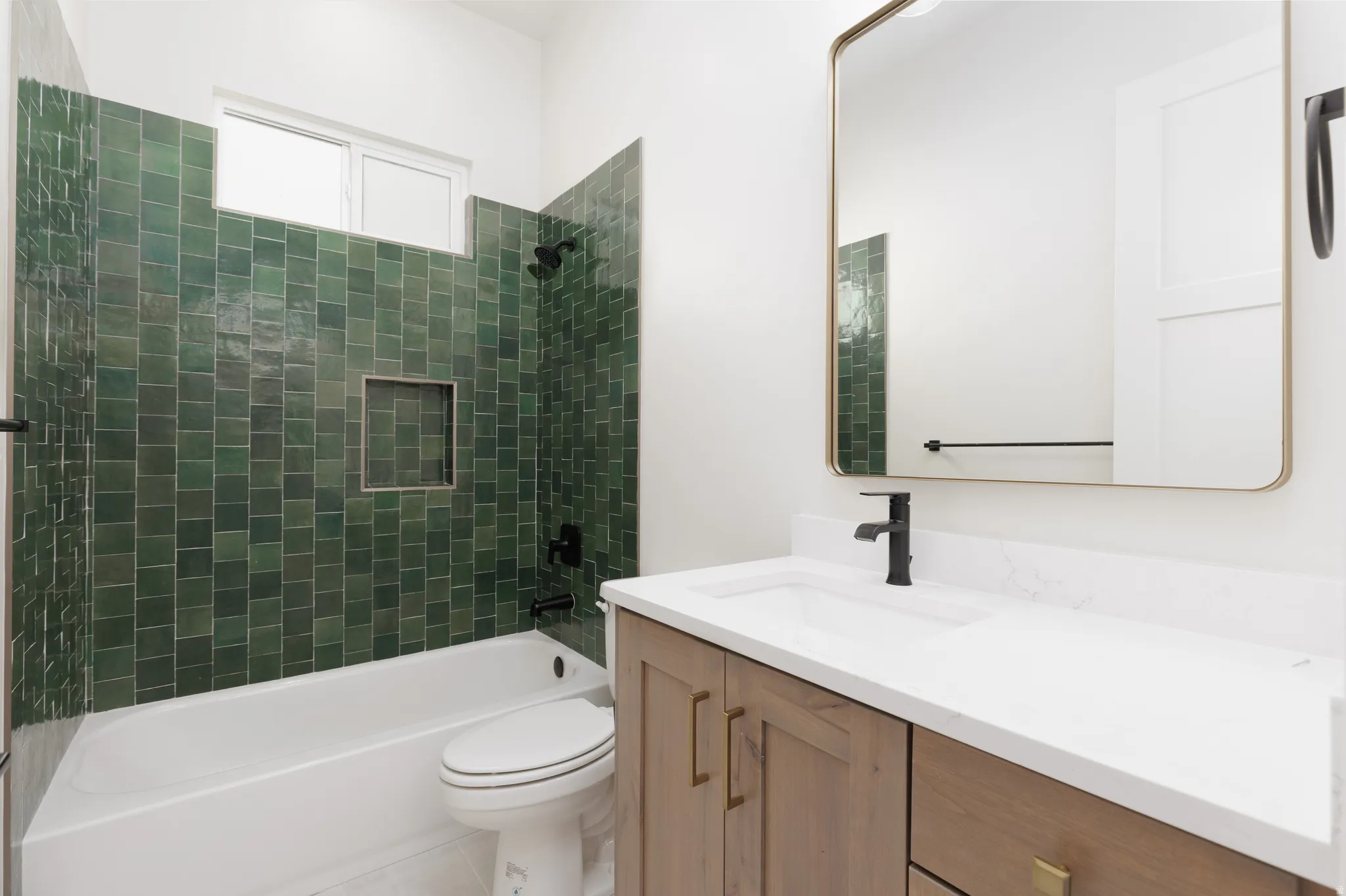 White bathtub with dark green subway tile surround, integrated shower niche, and black fixtures