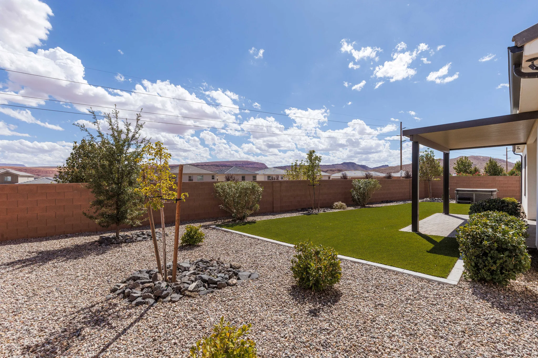 Landscaped backyard featuring artificial turf, a covered patio, a concrete block privacy wall, and gravel ground cover