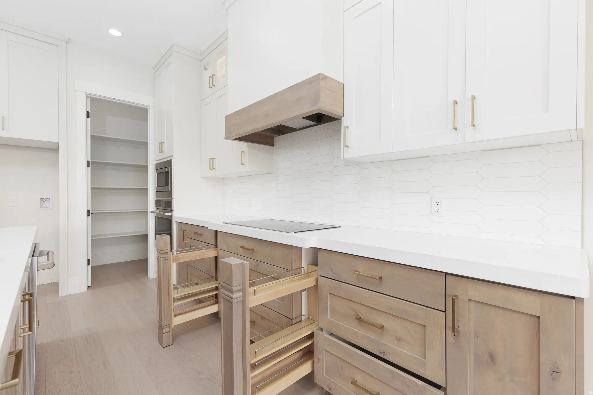 Gourmet kitchen with two-tone cabinetry, wood-finish flooring, white countertops, built-in oven and microwave, and walk-in pantry