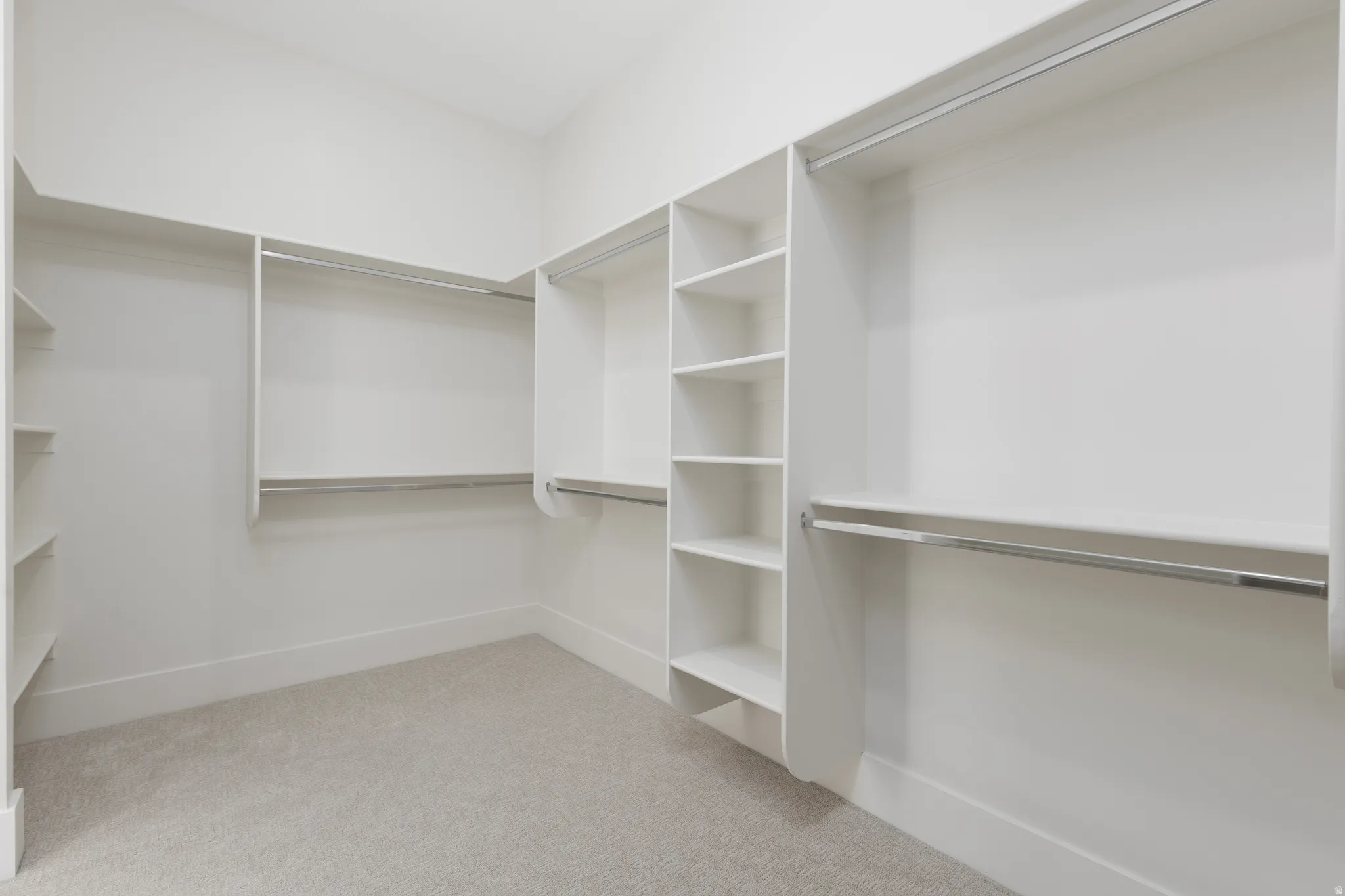 Walk-in closet featuring white built-in shelving, multiple hanging rods, and light-colored carpeting