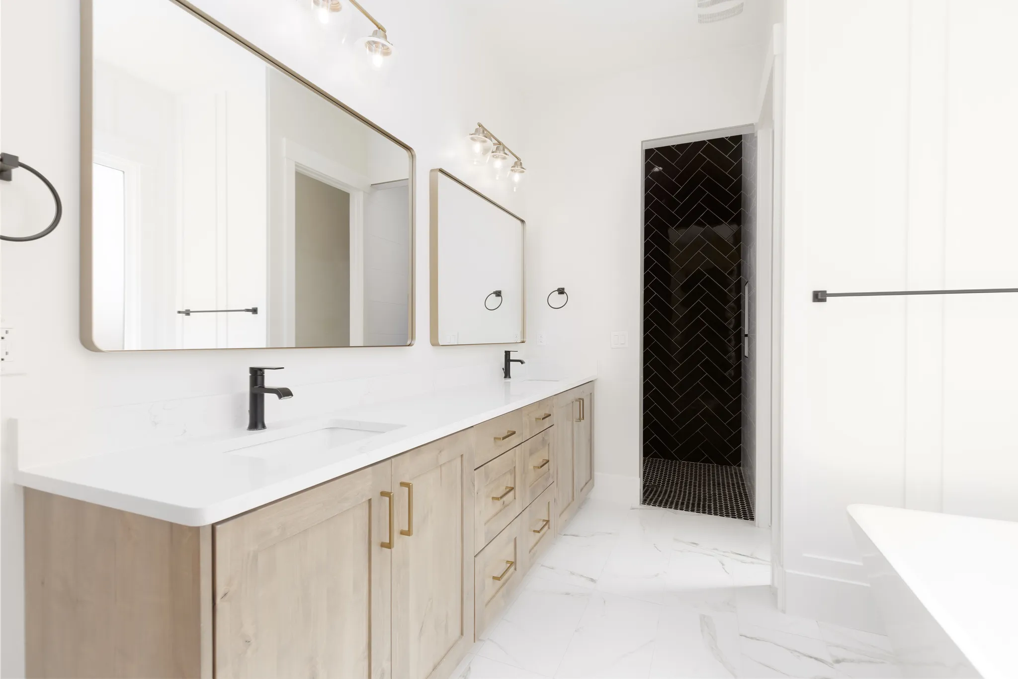 Dual vanity with light wood-finish cabinetry, white countertops, and matte black fixtures