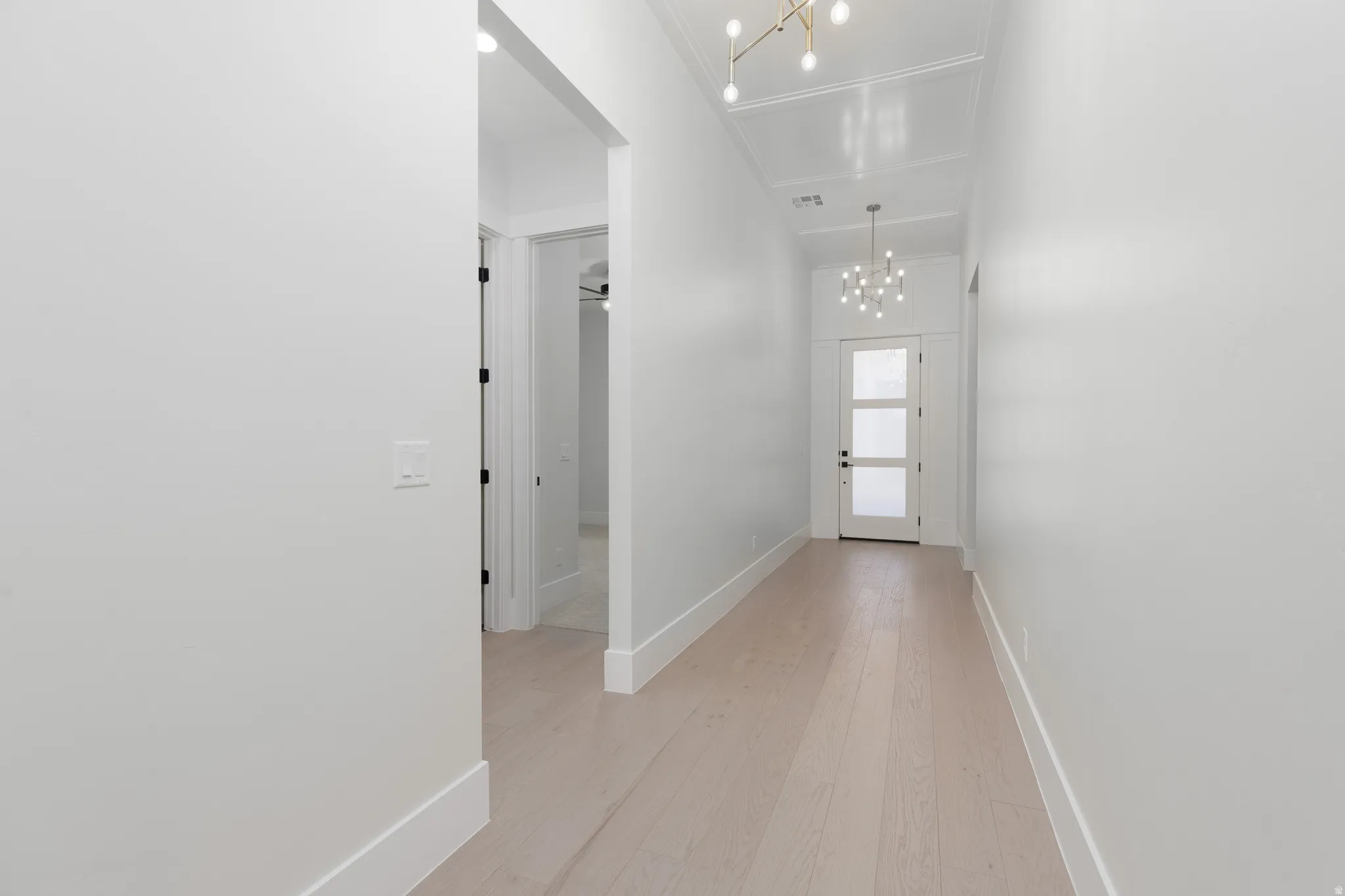 Recessed ceiling, wood-finish flooring, modern light fixtures, contemporary glass-paneled door, and white baseboards