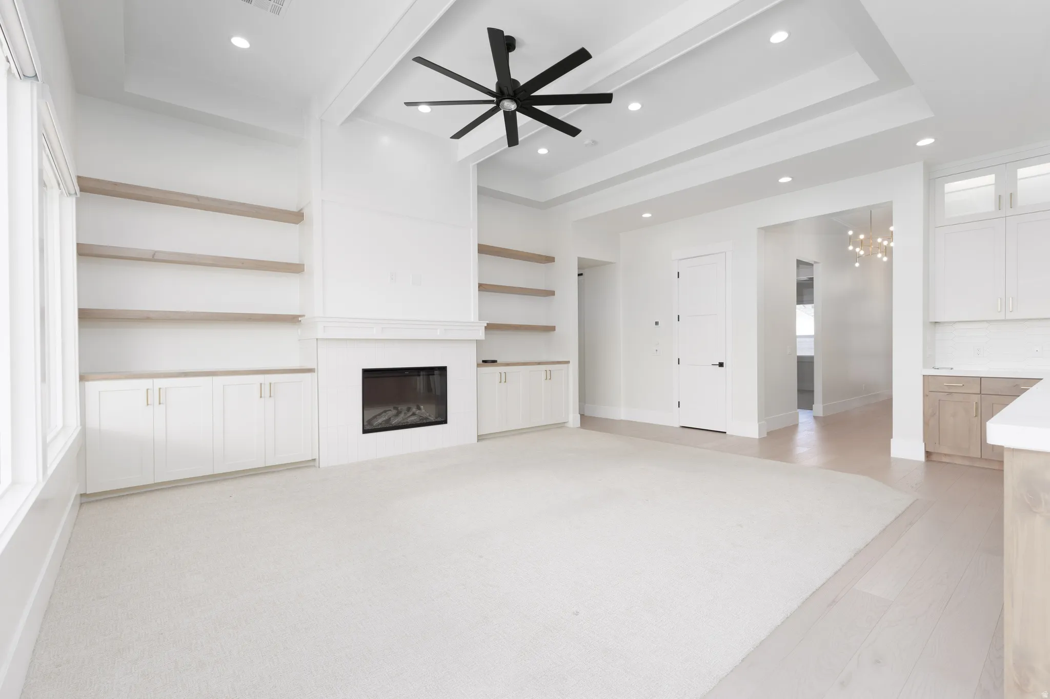 Spacious living area featuring a fireplace with a white mantel, built-in shelving, a tray ceiling with a ceiling fan, recessed lighting, and wood-finish flooring