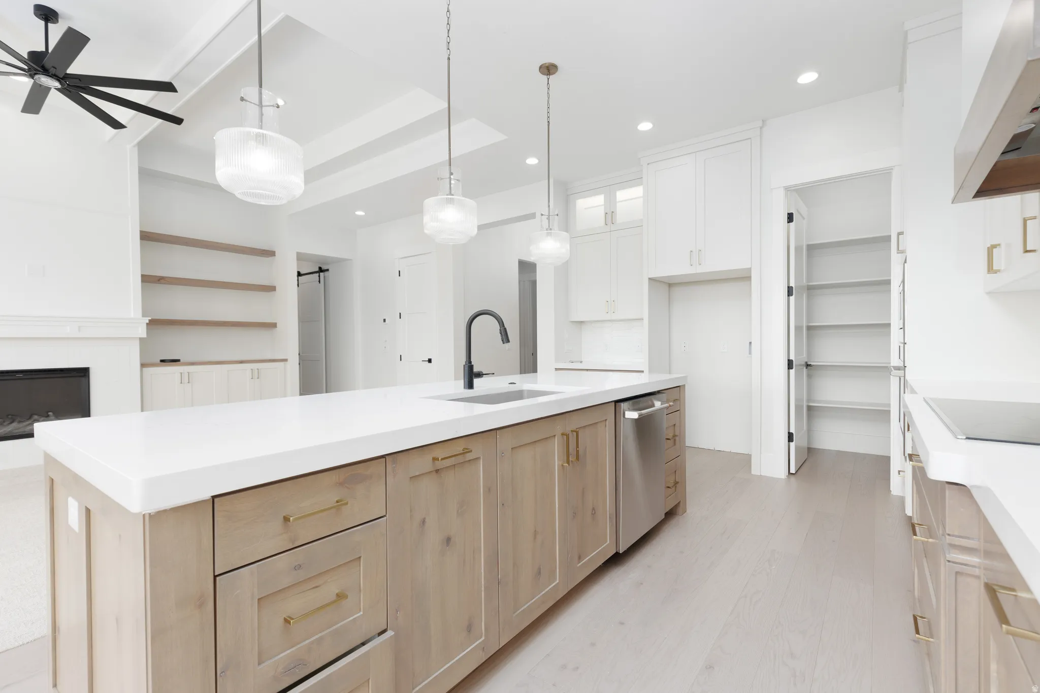 Kitchen island with a white countertop and wood-finish cabinetry, stainless steel dishwasher, and a black sink faucet