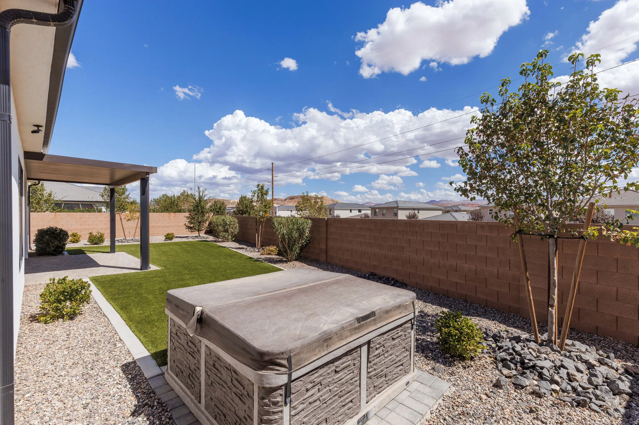 Expansive backyard featuring a covered patio, artificial turf lawn, decorative gravel, a spa, and a block wall perimeter