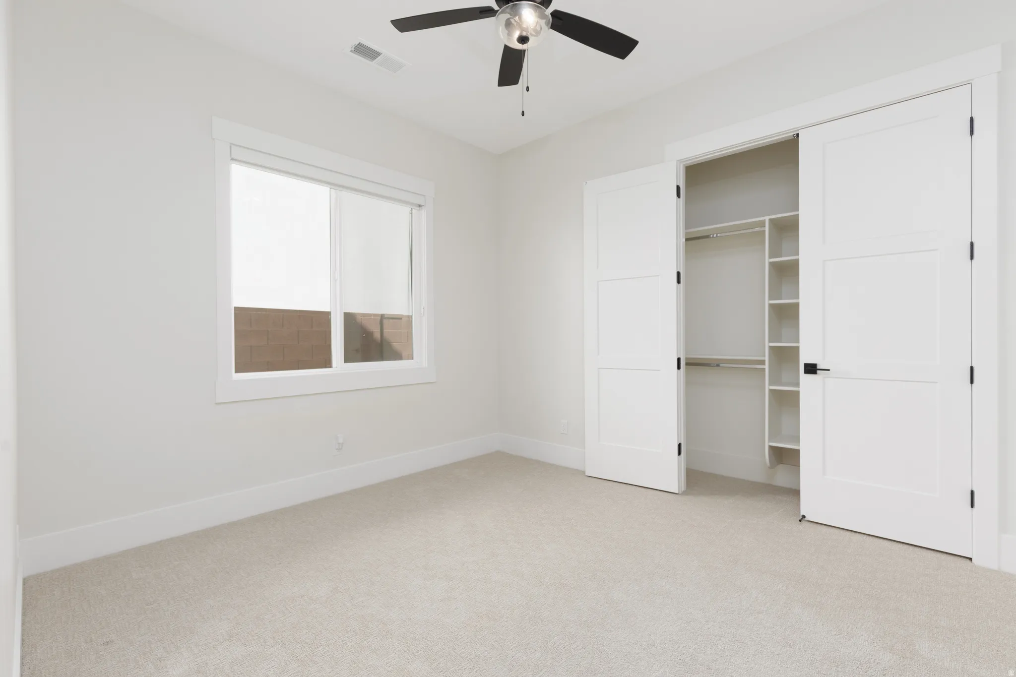 Neutral tone walls, ceiling fan with integrated lighting, window with white trim, built-in closet organization, and plush carpeting