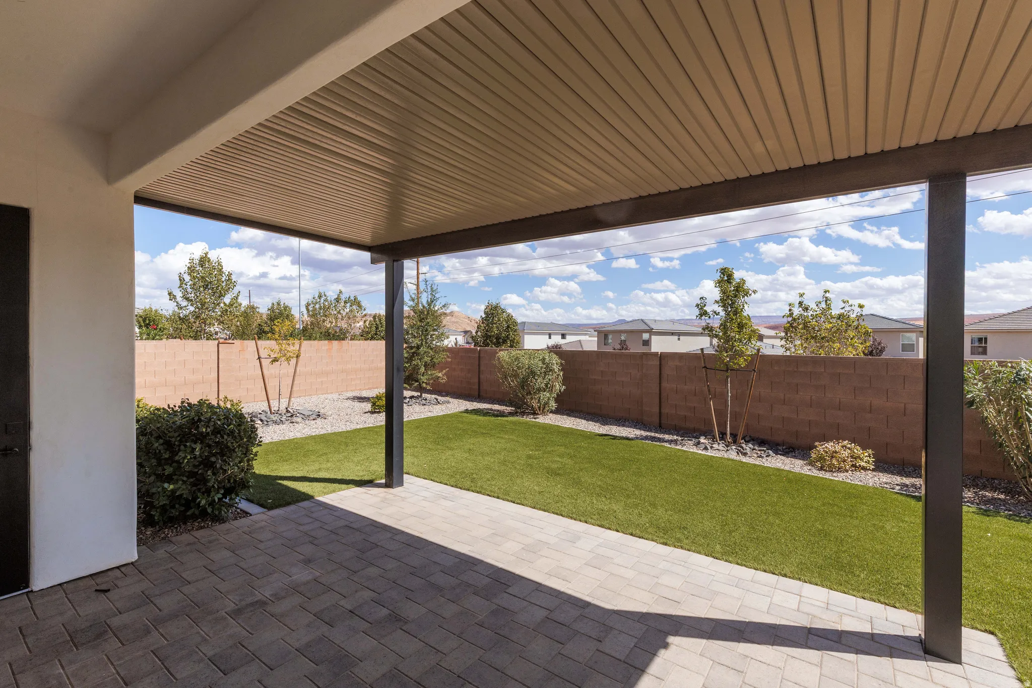 Covered patio with paver flooring, artificial turf, and a block fence