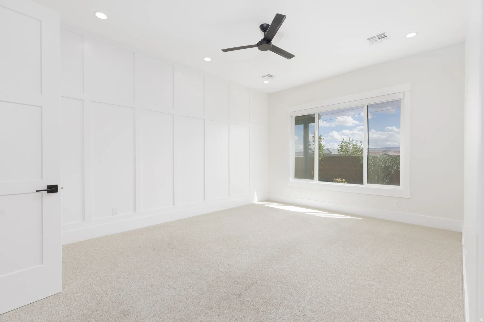 Recessed lighting, ceiling fan, expansive window, wall paneling, and neutral carpeting