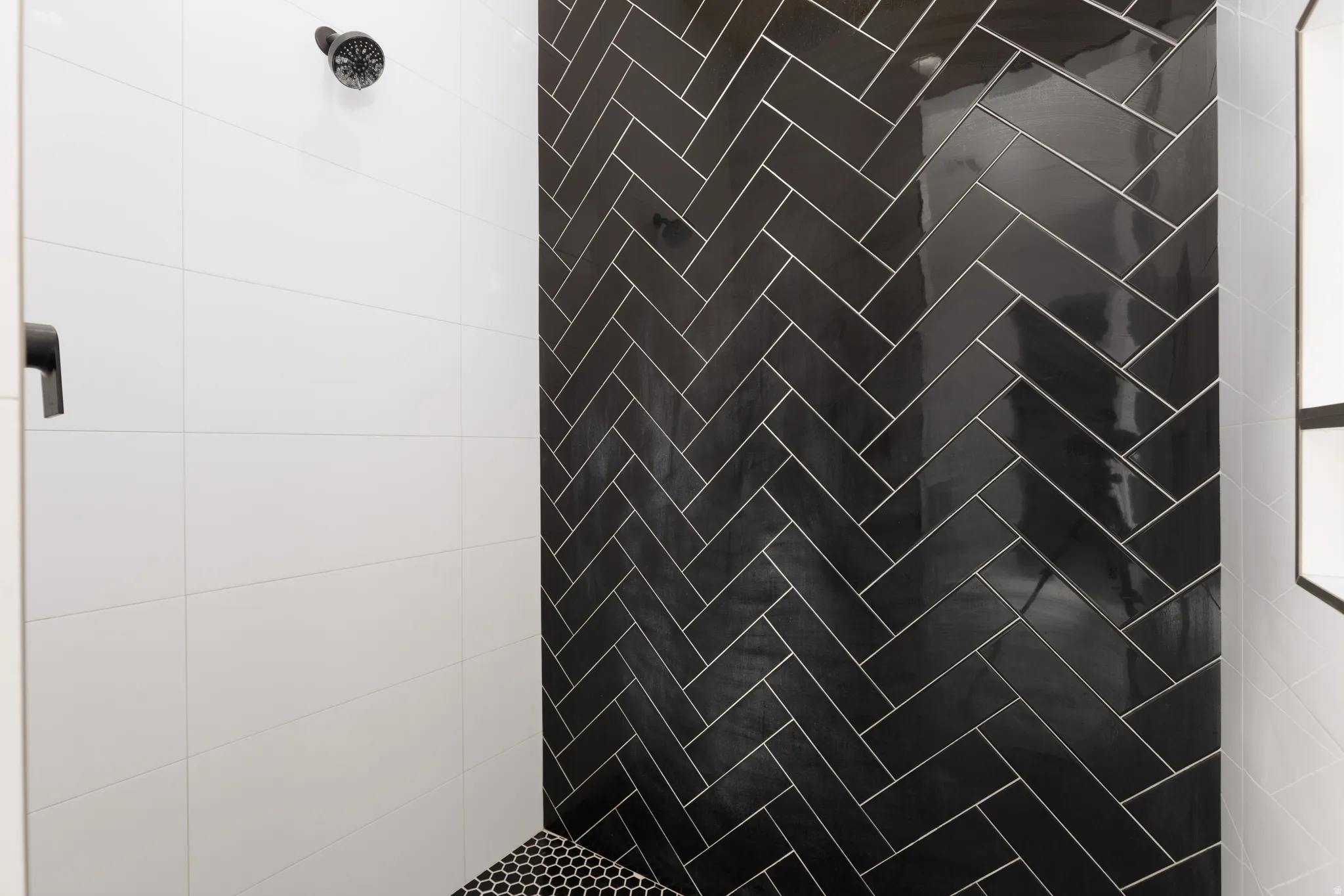 Black herringbone tile shower wall with white tiled walls and hexagonal mosaic floor