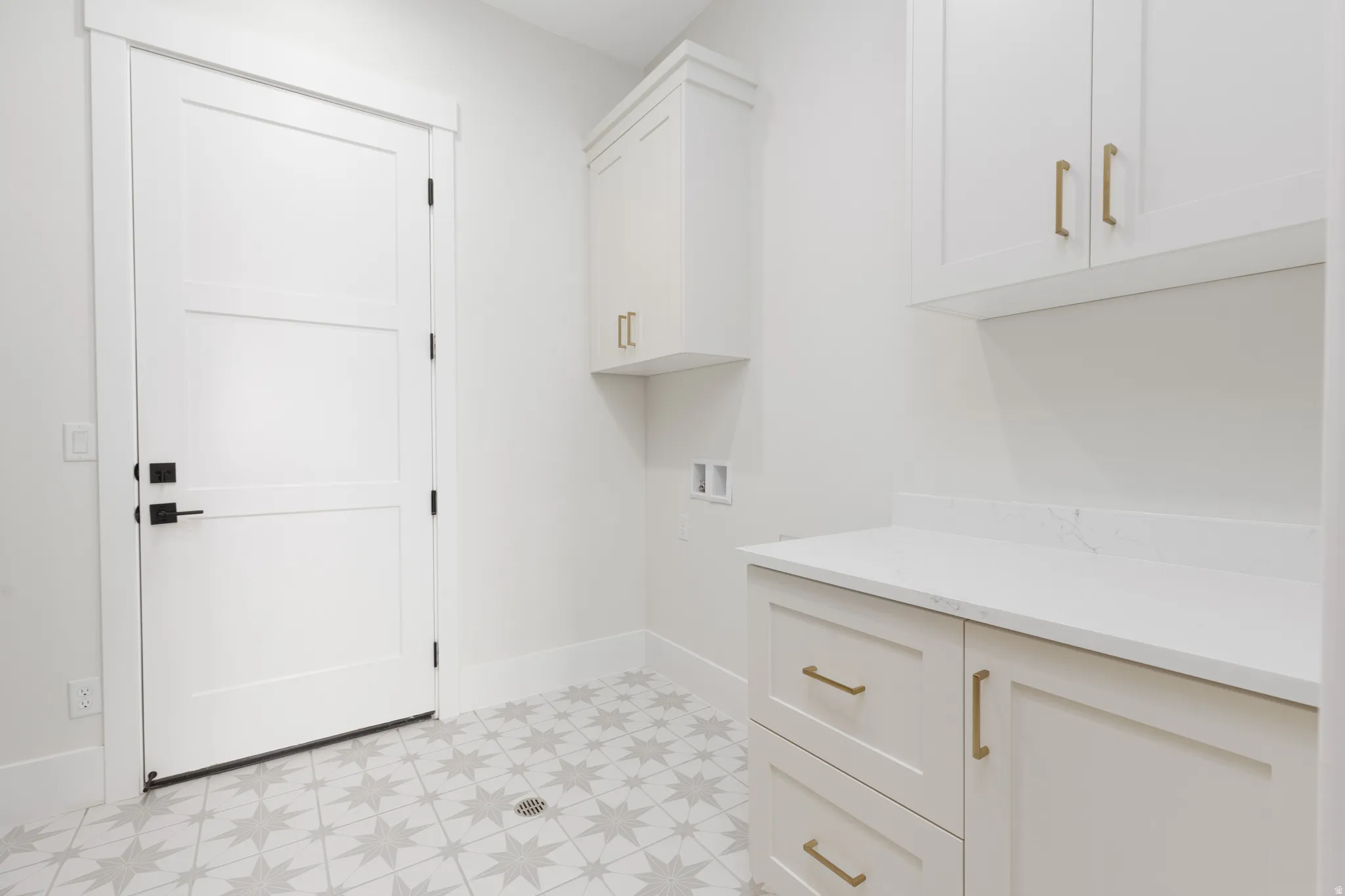 Bright utility space with patterned floor tiling, white cabinetry, integrated countertop, and matte black door hardware