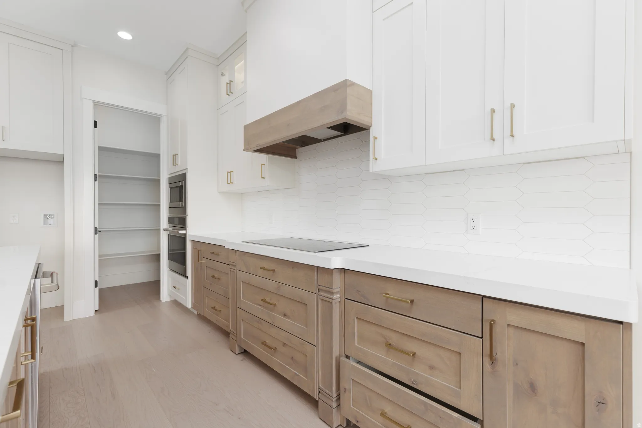 White upper cabinetry, wood-finish lower cabinetry, white solid surface countertops, white geometric tile backsplash, and wood-finish flooring