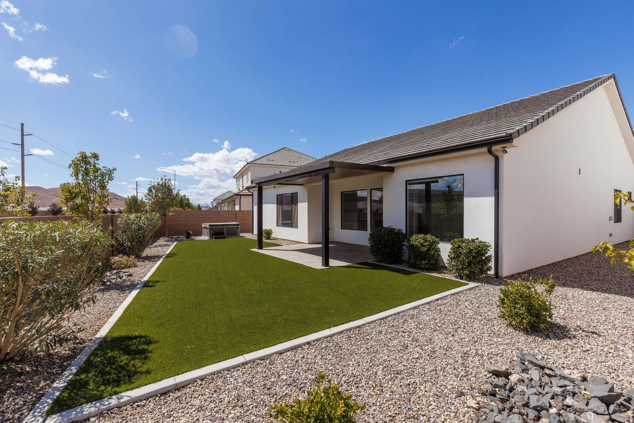 Rear exterior with a covered patio, artificial turf, and gravel landscaping