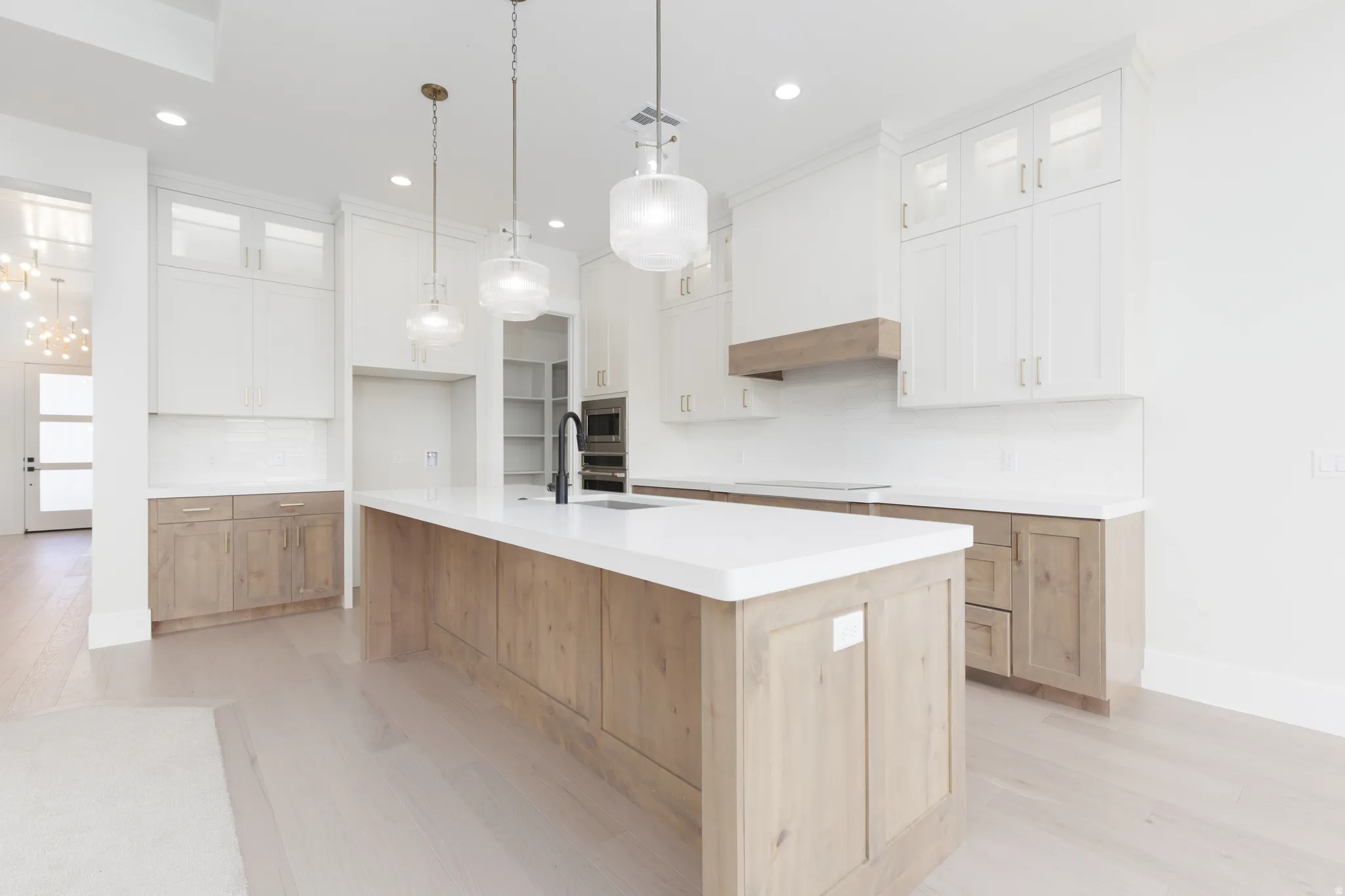 Expansive kitchen featuring a large central island with a white countertop, two-tone cabinetry with wood-finish base cabinets and white upper cabinets, stainless steel appliances, and recessed lighting