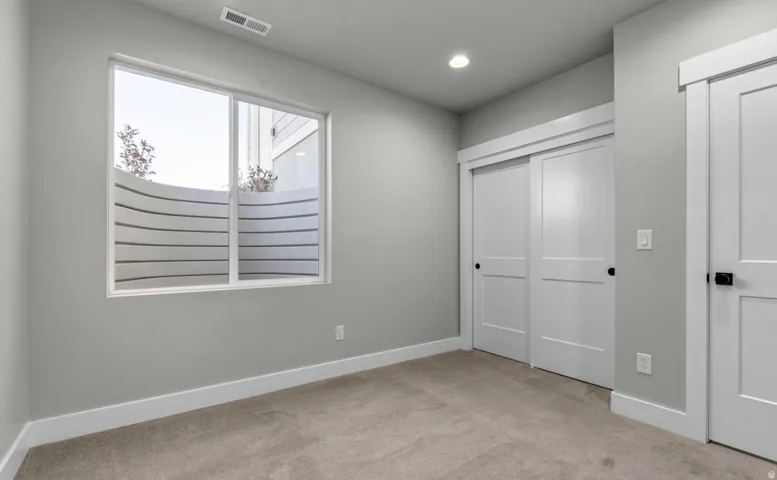 Carpeted flooring, recessed lighting, white trim, white sliding closet doors, and a window with a window well