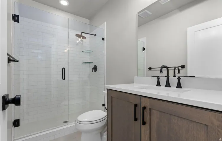 Walk-in shower with subway tile surround and glass enclosure, wood-finish vanity with an integrated sink, black hardware, and a large wall-mounted mirror