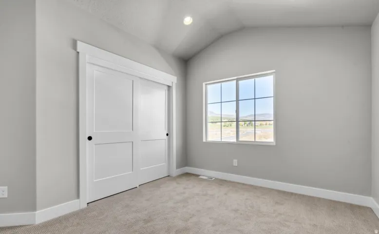 Vaulted ceiling, neutral wall paint, carpet flooring, window with grid pattern, double sliding closet doors