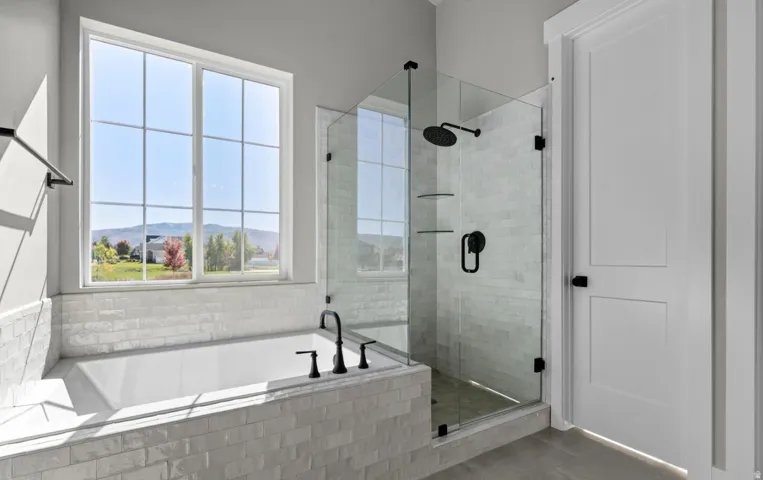 Built-in soaking tub with matte black fixtures, glass-enclosed shower with matte black showerhead, and a white paneled door