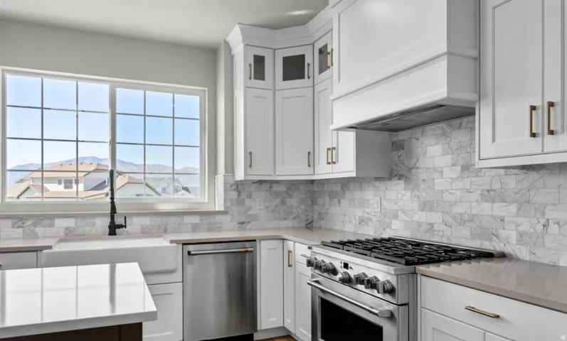 White shaker cabinetry, stone slab countertops, a stainless steel gas range, and a farmhouse-style sink