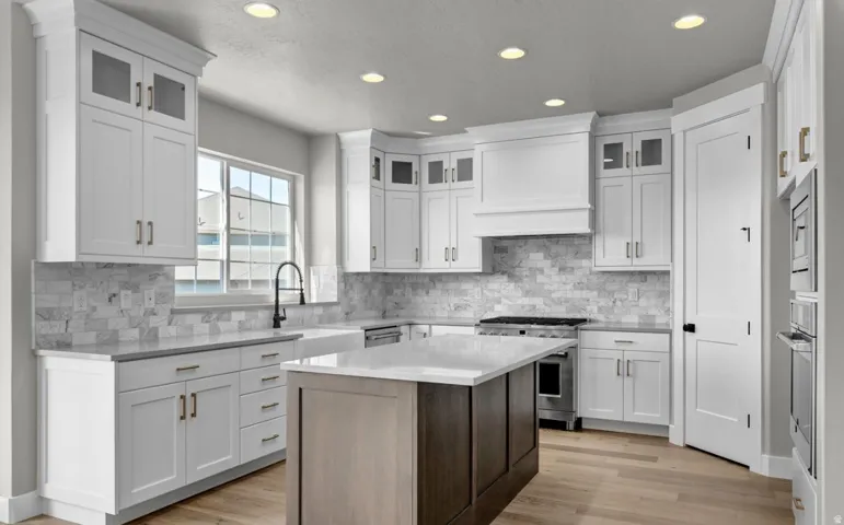 White shaker cabinetry, recessed lighting, wood-finish flooring, a kitchen island with a light-toned countertop, and a tile backsplash