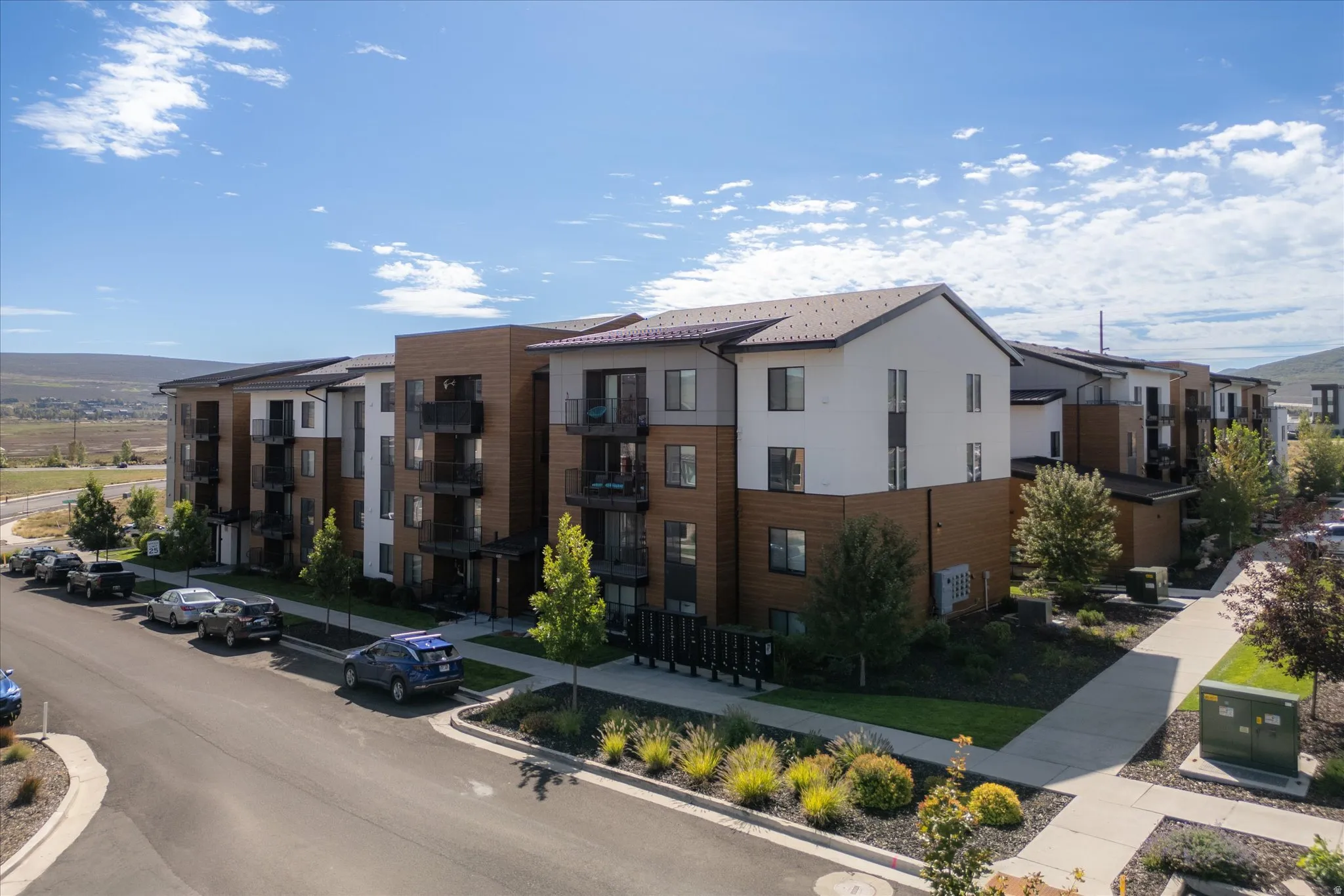 Multi-story residential building with contemporary architectural design, featuring private balconies, mixed-material facade, and landscaped grounds