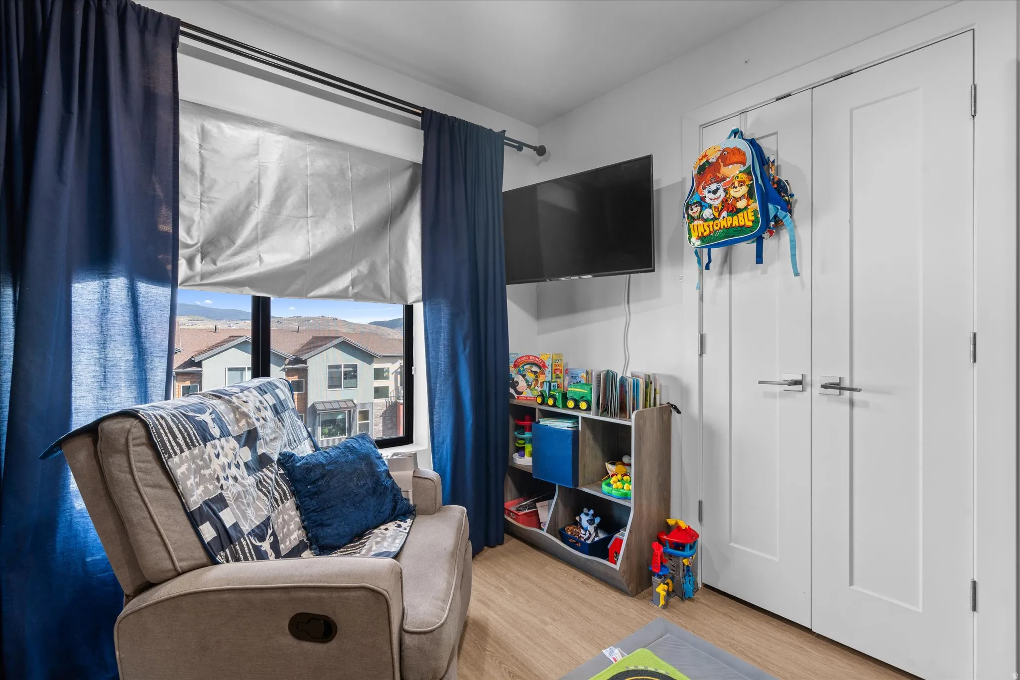 Recessed window with a roller shade, wood-finish flooring, and white bifold doors