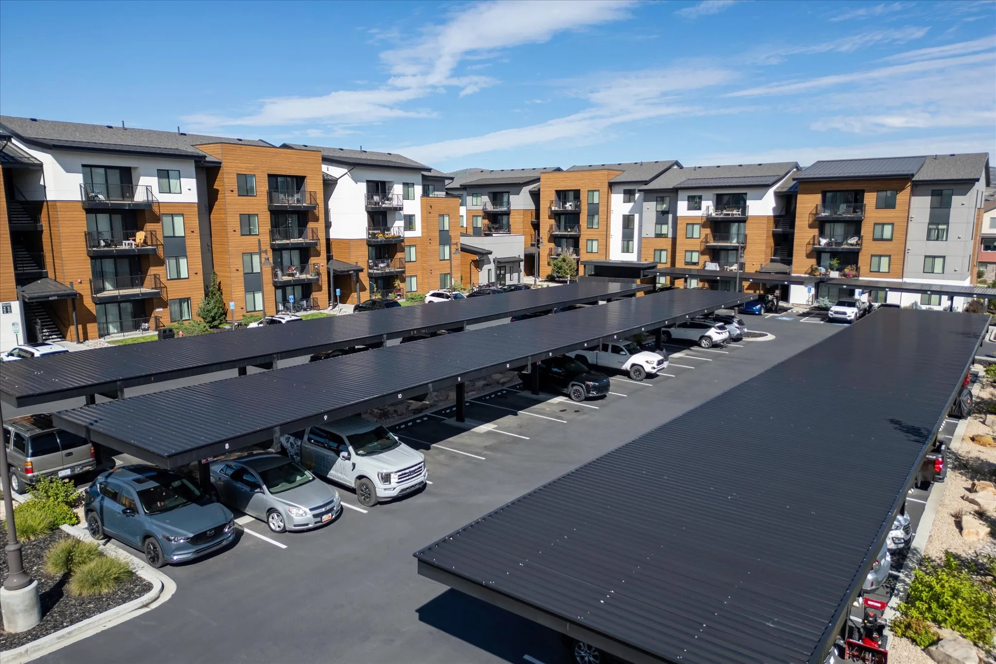 Multi-story residential buildings featuring private balconies and covered parking structures with ample spaces
