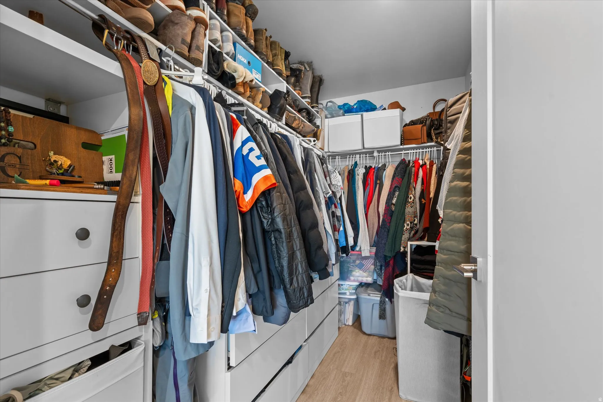 Custom closet system with multiple storage levels, white cabinetry, and wood-finish flooring