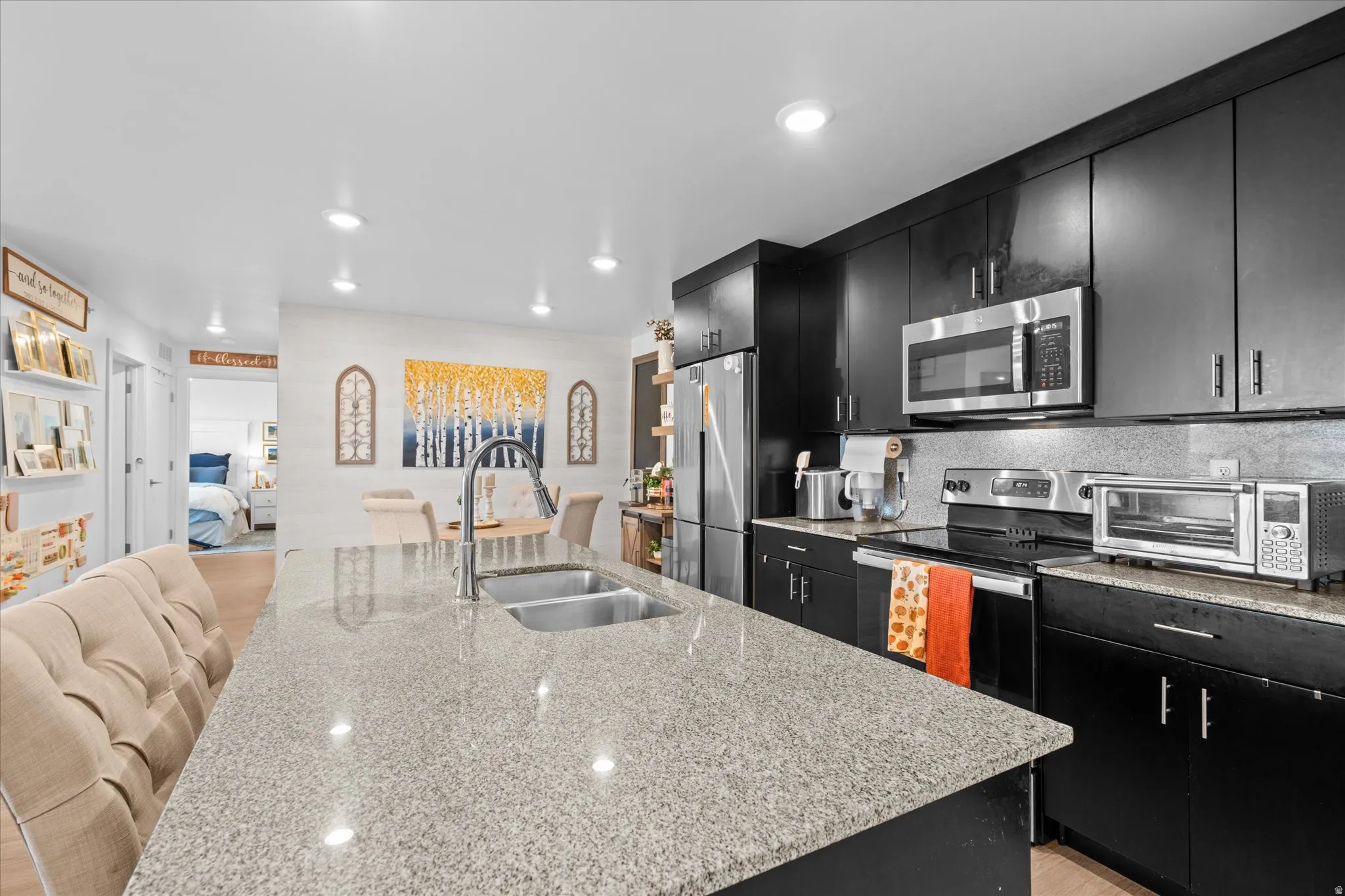 Kitchen featuring black cabinetry, stainless steel appliances, a double basin sink, and a spacious island with a light-colored countertop