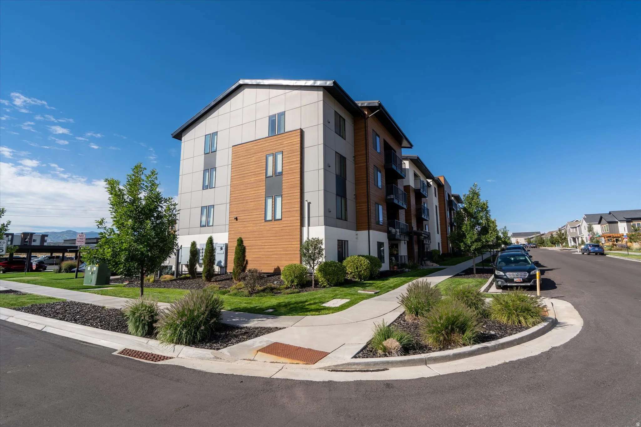 Modern exterior with horizontal wood-look siding accents, multi-pane windows, individual balconies, landscaped grounds, and a concrete sidewalk