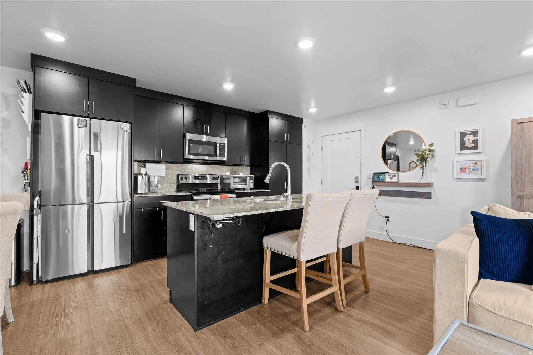 Modern kitchen with wood-finish flooring, dark cabinetry, and stainless steel appliances