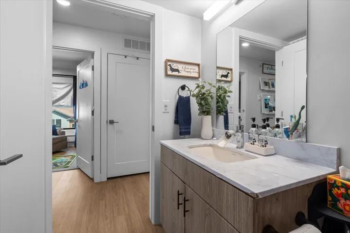 Wood-finish flooring, white solid core doors, wall-mounted mirror, vanity with a light-toned countertop, and modern cabinetry with dark hardware