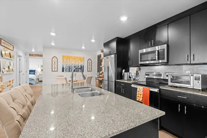Kitchen featuring black cabinetry, stainless steel appliances, a double basin sink, and a spacious island with a light-colored countertop