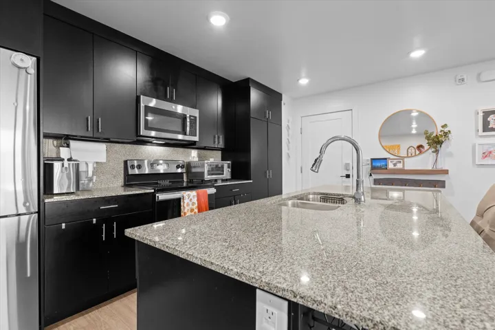 Kitchen featuring dark wood-finish cabinetry, light speckled countertops, stainless steel appliances, and an undermount sink with a gooseneck faucet